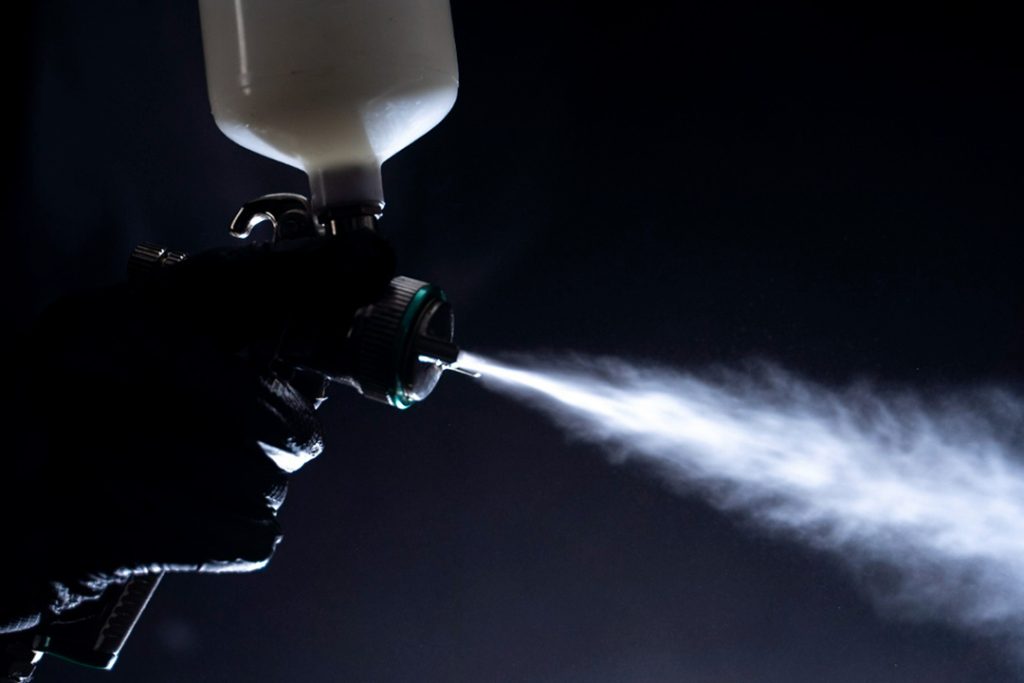 Dark photo of a spray gun shooting a mist of UV coating