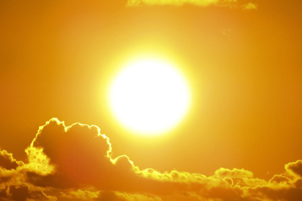 Yellow sunlight streaming from the white sun with clouds in the foreground