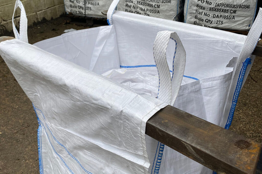 Forklift tines penetrating tunnel sleeves on a white bulk bag