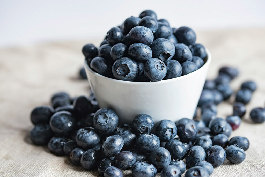 A large bunch of succulent blueberries in a white bowl on a wooden table.