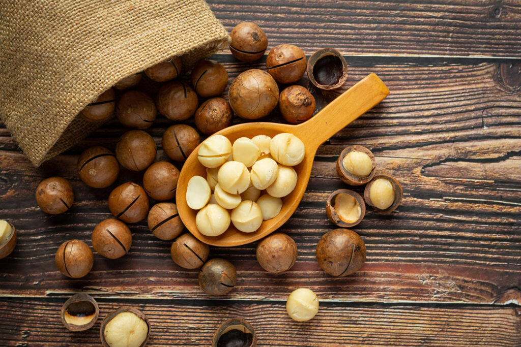 A pile of macadamia nuts spilling out of a hessian bag on a wooden surface.