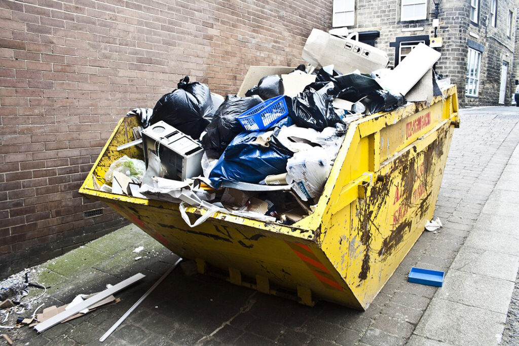 A full waste skip in an alley.