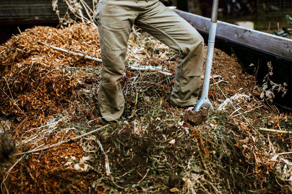 A person standing in a pile of garden waste with a pitch fork