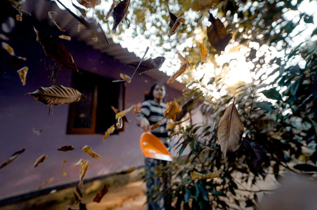 A woman throwing dried leaves out of a dustpan