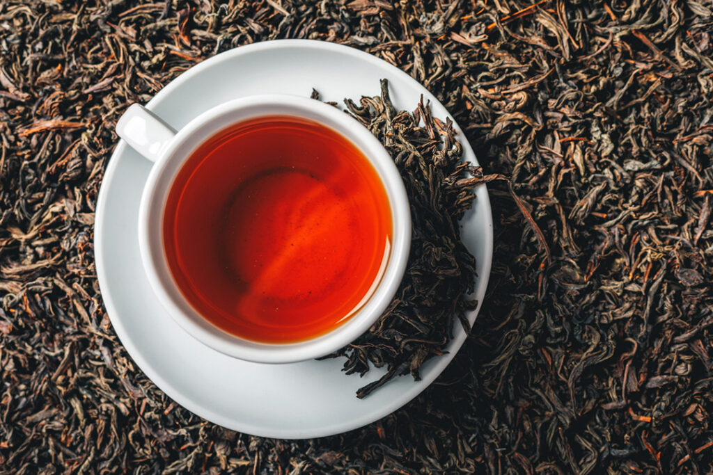 A cup of red tea surrounded by dried tea leaves