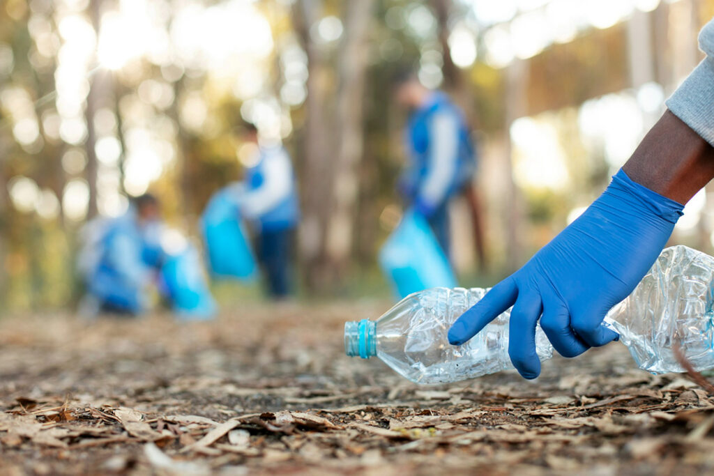 A man wearing blue rubber gloves picks up a plastic bottle in an outdoor setting.