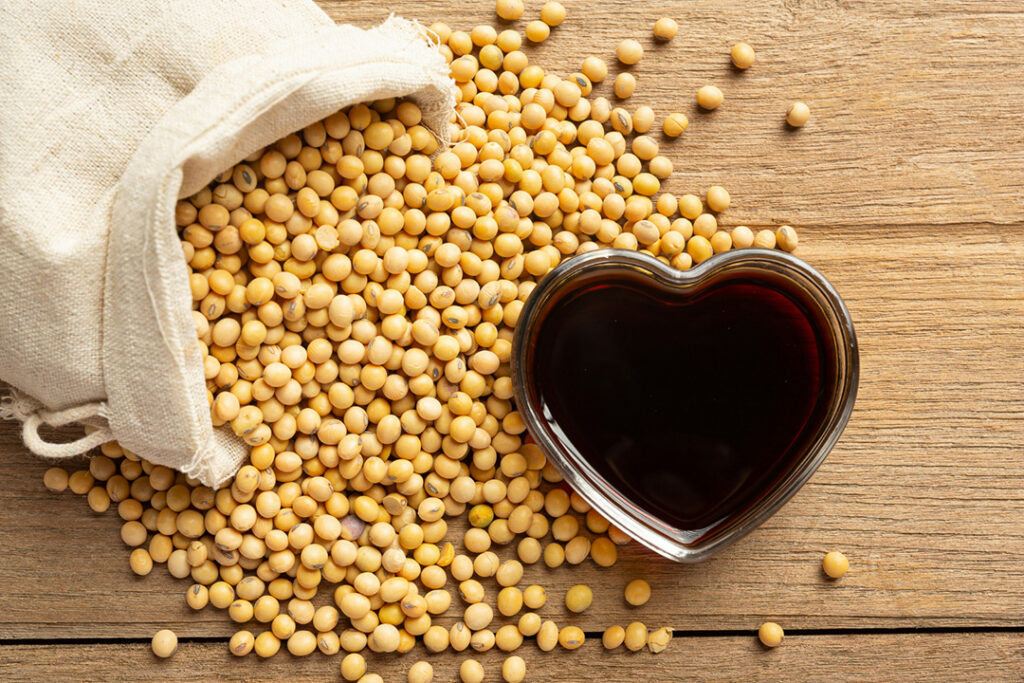 Dried soybeans spilling out of a cloth bag with a heart-shaped glass bowl filled with soy sauce
