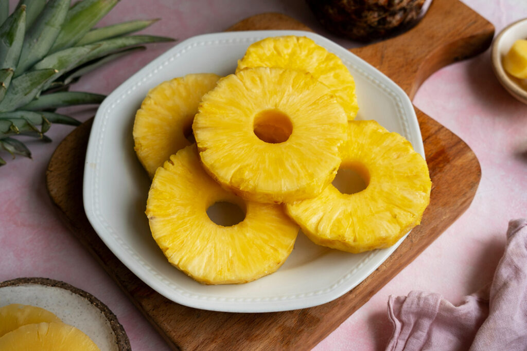Bright yellow slices of cored pineapple on a white plate.