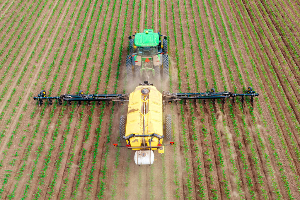 A green tractor spraying agricultural chemicals on a young crop in the ground.