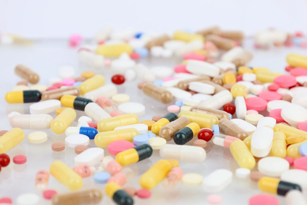Loose pharmaceuticals and multi-coloured pills on a glass tabletop.