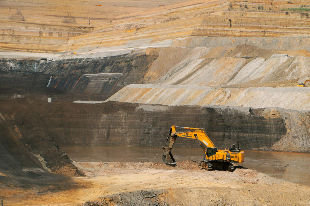 A yellow excavator working in a massive open pit mine.
